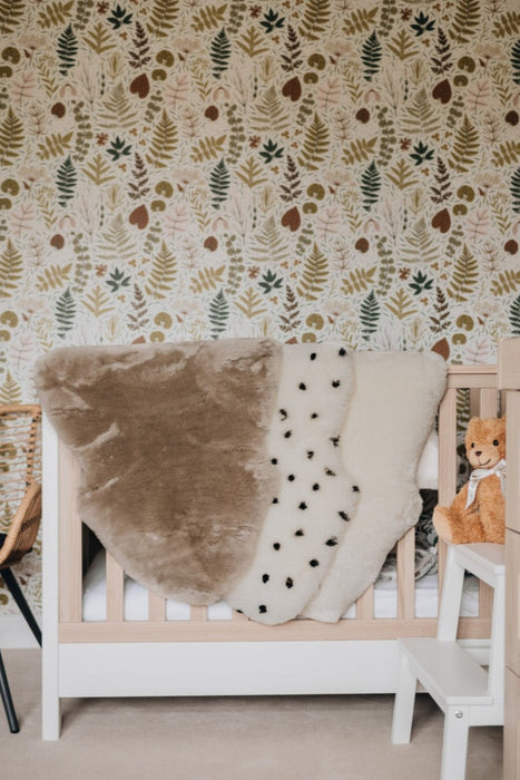 Sheepskin Nursing rugs in Toast, Spotted and Milk draped over a cot in a nursery