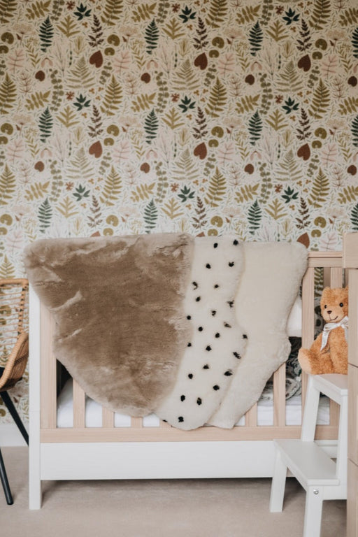 Sheepskin Nursing rugs in Toast, Spotted and Milk draped over a cot in a nursery