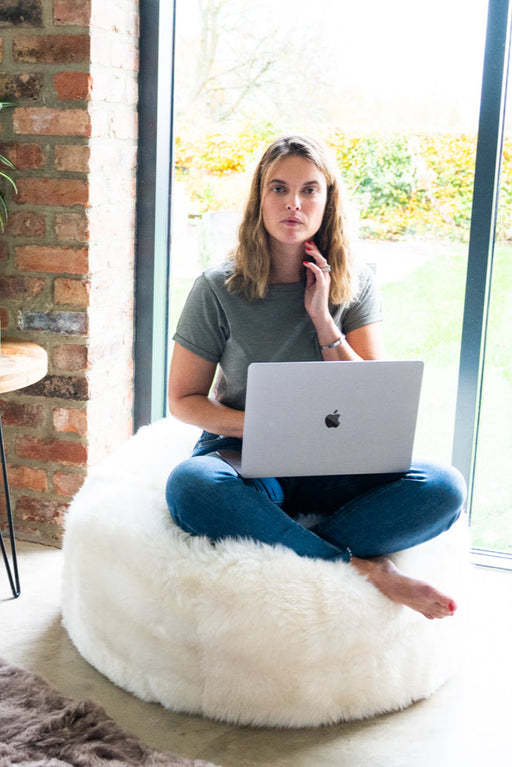 White Shorn Icelandic Sheepskin Bean Bag. Model sat cross legged on bean bag with computer.