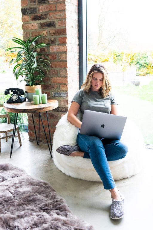 White Shorn Icelandic Sheepskin Bean Bag. Model sat cross legged on bean bag with computer.