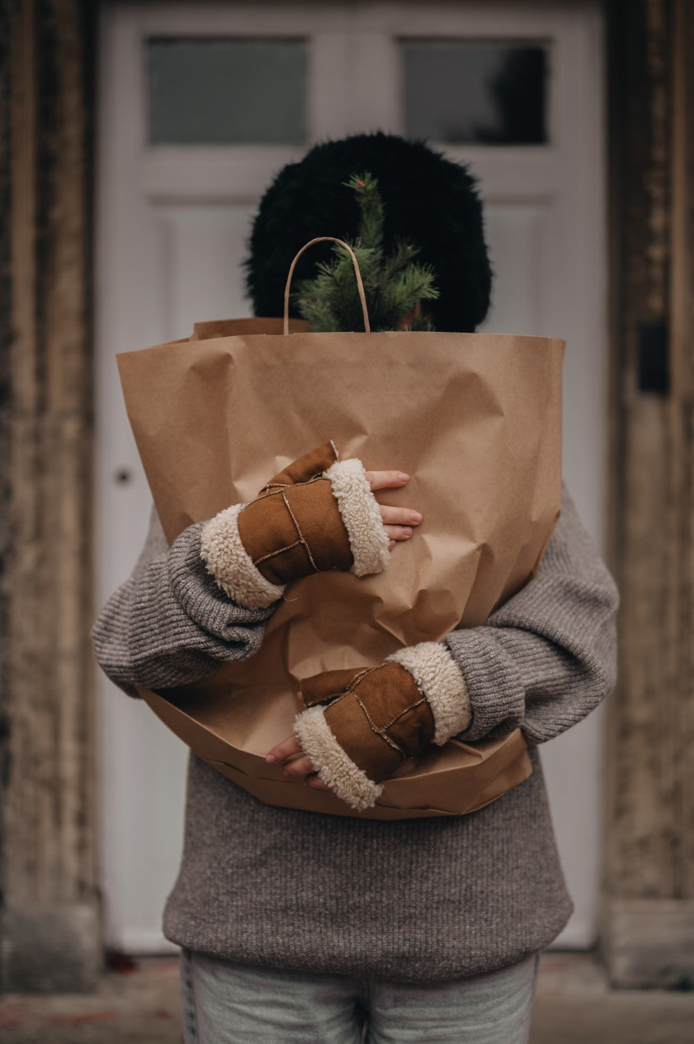 woman holding paper bag wearing sheepskin fingerless mittens